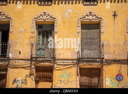 Facciata di un vecchio edificio con balconi e finestre molto deteriorate, con graffiti e crepe sulla facciata gialla Foto Stock