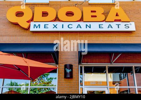 Il Qdoba Mexican mangia la facciata esterna del ristorante, il marchio e il logo in lettere arancioni sopra le finestre di vetro delle tende nere e l'ombrello arancione. Foto Stock