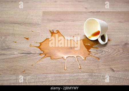 Una tazza di caffè cadde sul laminato, il caffè versato sul pavimento. Concentratevi sulla pozzanghera. Foto Stock
