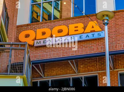 Il Qdoba Mexican mangia la facciata esterna del ristorante e la segnaletica con logo in lettere arancioni su mattoni rossi sotto le finestre riflettenti con lampione. Foto Stock