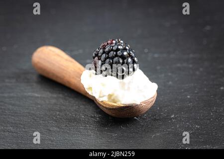 mora con crema su un cucchiaio pronto da mangiare Foto Stock