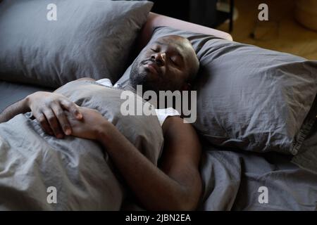 Alto angolo di vista di afroamericano bearded uomo che riposa e dorme nel suo letto in camera da letto Foto Stock