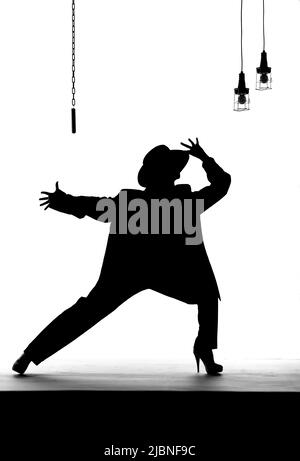 Una ballerina femminile balla su un vecchio palcoscenico logoro. Vestito di abbigliamento maschile, indossando un cappello da uomo si vede ballare come una silhouette. Foto Stock