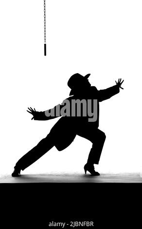 Una ballerina femminile balla su un vecchio palcoscenico logoro. Vestito di abbigliamento maschile, indossando un cappello da uomo si vede ballare come una silhouette. Foto Stock