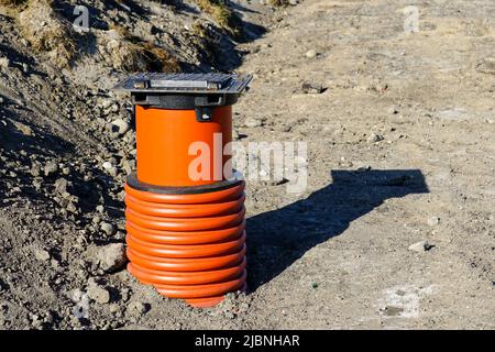 Nuovo pozzo di drenaggio dell'acqua piovana con coperchio in ferro nero e tubo fognario in plastica marrone in un nuovo cantiere Foto Stock