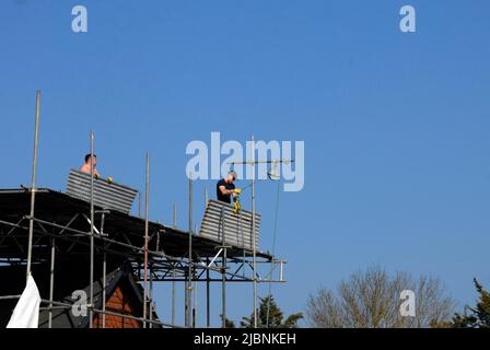 Due uomini che rimuovono le lenzuola di ferro ondulato dalla copertura temporanea del tetto sulla casa di nuova costruzione Foto Stock