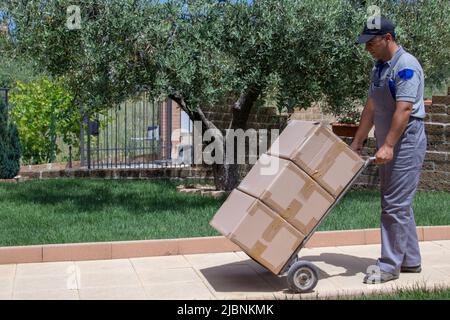 Immagine di un ragazzo di consegna che trasporta grandi pacchi con un carrello in una casa Foto Stock