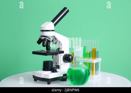 Microscopio moderno e vetreria da laboratorio su tavolo vicino a parete verde Foto Stock