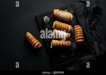 tubuli al forno riempiti con panna bianca montata su un tavolo da cucina in legno nero, vista dall'alto Foto Stock