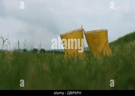 Stivali di gomma gialli lasciati nel mezzo del campo. Stivali in gomma che rimangono sull'erba Foto Stock