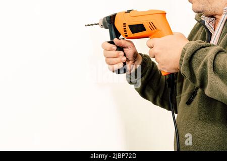 Lavoro di costruzione che fora un buco con un trapano su una parete bianca. Spazio di copia. Foto Stock