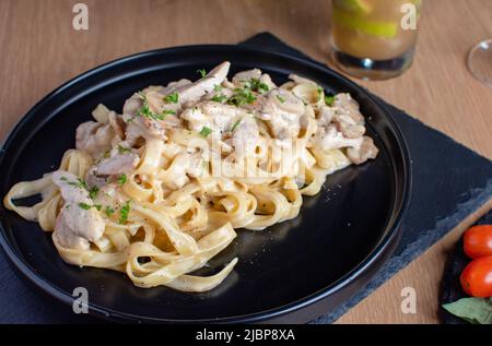 Pasta di pollo Alfredo con salsa bianca in un piatto nero Foto Stock