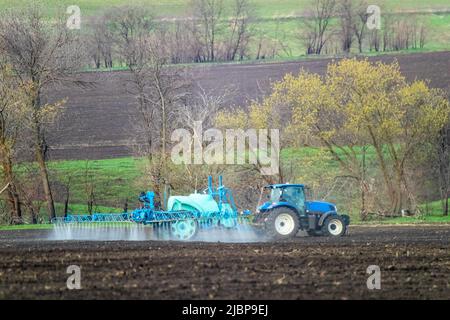 Trattore che spruzza insetticida su campo di terra coltivato. Macchine agronomiche agricole in funzione in una giornata di primavera. Vista sulla campagna Foto Stock