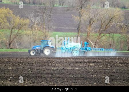 Trattore che spruzza insetticida su campo di terra coltivato. Attrezzature agronomiche agricole in funzione in una giornata di primavera. Paesaggio rurale Foto Stock