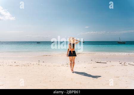 NUNGWI, Zanzibar, Tanzania: Donna che indossa un cappello da sole che cammina sulla spiaggia con bassa marea. Foto Stock