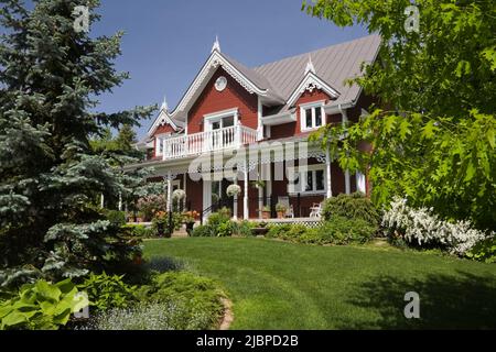 Borgogna con finiture bianche Casa vittoriana stile cottage delimitato da Spiraea x vanhouttei 'Van Houtte' - Spirea, Syringa vulgaris - Lilac albero in primavera. Foto Stock