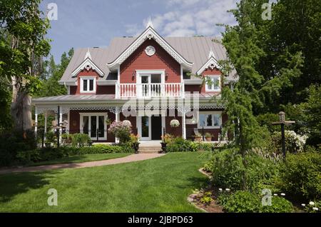 Borgogna con finiture bianche Casa vittoriana stile cottage delimitato da Spiraea x vanhouttei 'Van Houtte' - Spirea, Syringa vulgaris - Lilac albero in primavera. Foto Stock