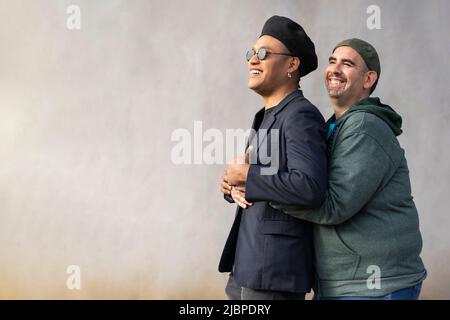 Coppia latina gay che indossa cappelli alla moda abbracciano la strada. Spazio di copia Foto Stock