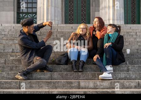 Gruppo multietnico di amici seduti su alcune scale che si divertono a chiacchierare, ridere e scattare foto Foto Stock