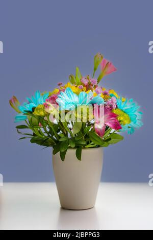 Piccolo bouquet di crisantemi gialli e blu su un tavolo bianco, sfondo scuro. Foto Stock