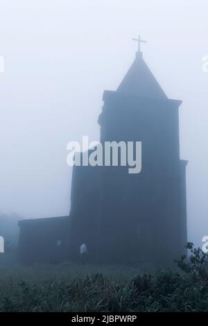 Un uomo cammina verso la chiesa cattolica abbandonata nella nebbia, la chiesa è stata costruita dai francesi nel 1928. Monti Damrei, Kampot, Cambogia. Foto Stock