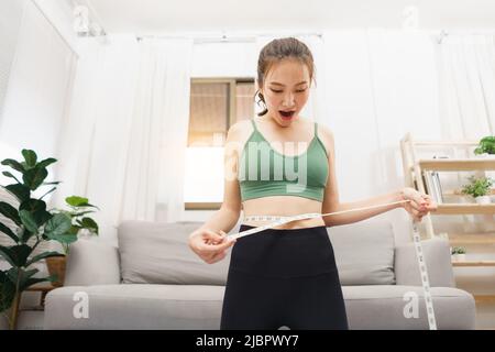 Concetto sano e di perdita di peso, giovane donna asiatica eccitata mentre misurando la vita con metro a nastro. Foto Stock