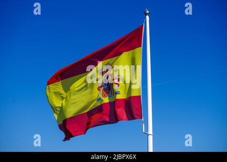 Bandiera nazionale della Spagna che vola al vento di fronte al cielo azzurro Foto Stock
