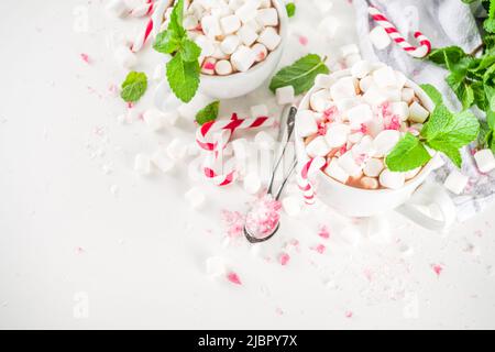 Cioccolata calda alla menta piperita fatta in casa. Due tazze di bevanda calda al cacao, con menta, marshmallow e canna da zucchero, su sfondo bianco del tavolo Foto Stock