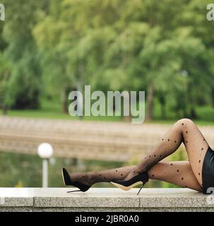 Gambe femminili sottili in collant con motivo a cuore in profilo con parco cittadino sullo sfondo Foto Stock