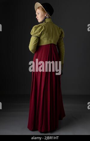 Una donna Regency che indossa uno spencer in lino verde e un abito rosso con un cofano Foto Stock