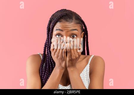 Ritratto di spaventato giovane afroamericana che copre il suo volto con le mani su sfondo rosa studio Foto Stock