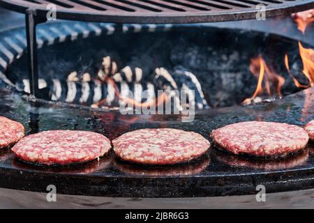 I polpettine di hamburger crudi vengono grigliati al barbecue sul fuoco aperto nel parco. Foto Stock