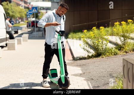 Mobilità verde trasporto sostenibile. Uomo nero moderno sbloccare e-scooter con il suo cellulare, a piedi in città Foto Stock