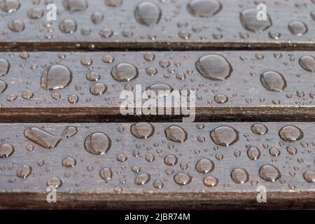 Tavole di legno coperte da gocce d'acqua, sfondo per il tempo piovoso. Tavole marroni bagnate in primo piano. Messa a fuoco selettiva Foto Stock