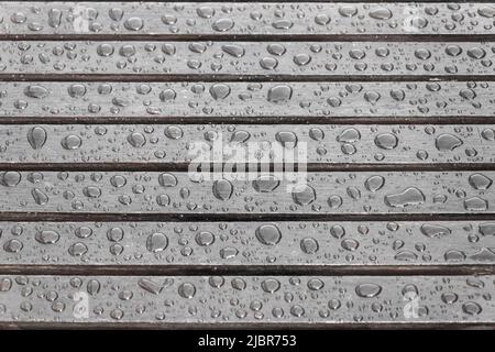 Tavole di legno coperte da gocce d'acqua, sfondo per il tempo piovoso. Tavole marroni bagnate in primo piano. Messa a fuoco selettiva Foto Stock