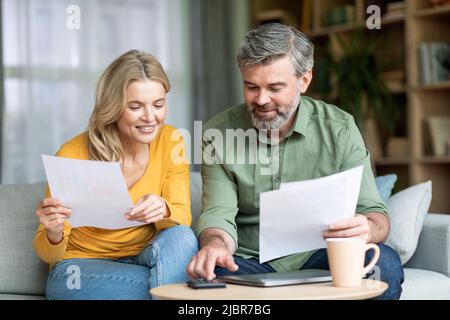 Coniugi di mezza età che controllano la documentazione finanziaria mentre pianificano il budget familiare a casa Foto Stock