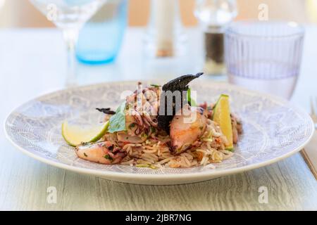 Calamari fritti in padella e riso aromatizzato in stile orientale con fettine di lime e foglie di basilico Foto Stock