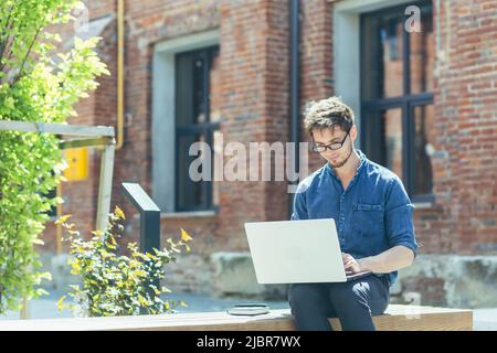 Giovane studente al campus che studia e lavora online su laptop, uomo in abiti casual fuori ufficio Foto Stock