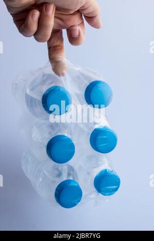 Sei piccole bottiglie di plastica di acqua naturale di sorgente appesi al dito sullo sfondo bianco.immagine verticale Foto Stock