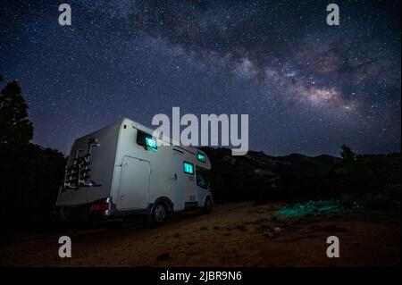 Camper RV parcheggiato sotto stelle su un molo vicino al mare, Creta, Grecia. I viaggiatori con camper riposano durante la notte sotto la via lattiginosa su una famiglia attiva Foto Stock
