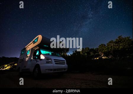 Camper RV parcheggiato sotto stelle su un molo vicino al mare, Creta, Grecia. I viaggiatori con camper riposano durante la notte sotto la via lattiginosa su una famiglia attiva Foto Stock