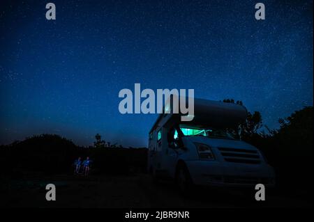 Camper RV parcheggiato sotto stelle su un molo vicino al mare, Creta, Grecia. I viaggiatori con camper riposano durante la notte sotto la via lattiginosa su una famiglia attiva Foto Stock