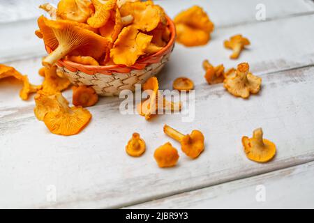 Chanterelle di funghi arancioni in un cestino di vimini su un tavolo di legno bianco. Foto Stock