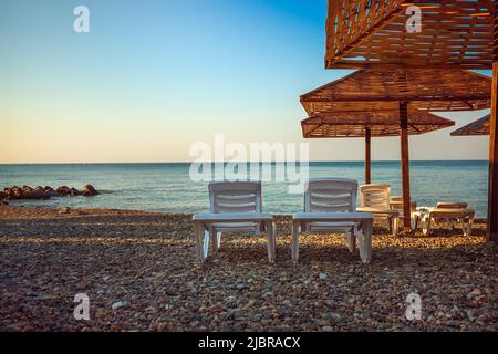 un paio di lettini con un ombrello sullo sfondo del mare all'alba. spazio copia. Foto Stock
