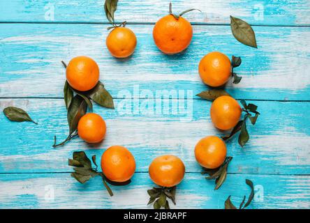 Tangerini con foglie verdi sul frutto e sulla tavola, giacenti in cerchio su una tavola di legno blu. La vista dall'alto. Foto Stock