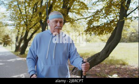 Allegro anziano anziano 80s uomo caucasico nonno allenamento Nordic Walk con bastoncini da trekking sci nel parco estivo all'aperto. Escursioni tempo libero hobby. Pensionato anziani maturi motivazione sportiva sana Foto Stock
