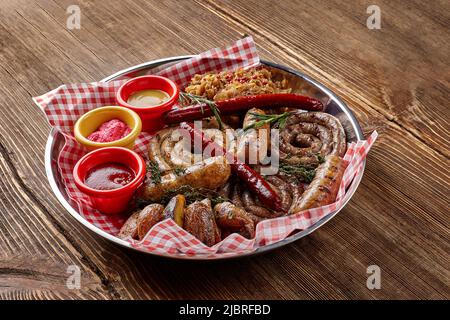Diversi tipi di salsicce alla griglia con salse, patate e cavolo diversi in piatto su un tavolo di legno. Foto Stock