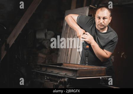 Un uomo perfora il metallo con un trapano a mano nella sua officina domestica. Realizzare un prodotto in metallo con le proprie mani Foto Stock