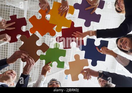 I gioiosi impiegati maschili e femminili hanno messo insieme pezzi colorati di puzzle a riunione in ufficio. Foto Stock