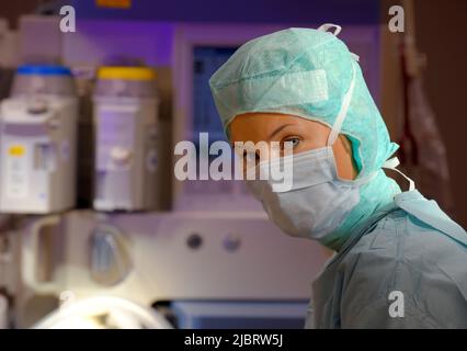 Una donna è vista in un teatro di funzionamento dell'ospedale. È completamente vestita come infermiera anestetica con una maschera facciale e indumenti chirurgici medici sterili. Foto Stock